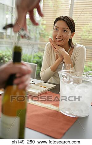 Close-up of a person's hand opening a wine bottle with a young woman sitting at the dining table View Large Photo Image Stock Image - Close-up of a person's hand opening a wine bottle with a young woman sitting at the dining table. Fotosearch