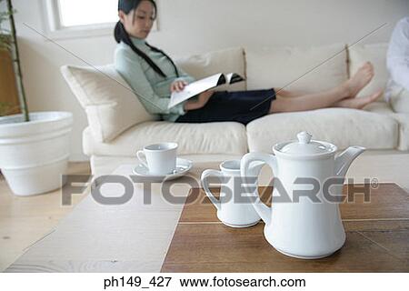 Close-up of a tea kettle on the table with a young woman sitting on a couch in the background View Large Photo Image Stock Photo - Close-up of a tea kettle on the table with a young woman sitting on a couch in the background. Fotosearch