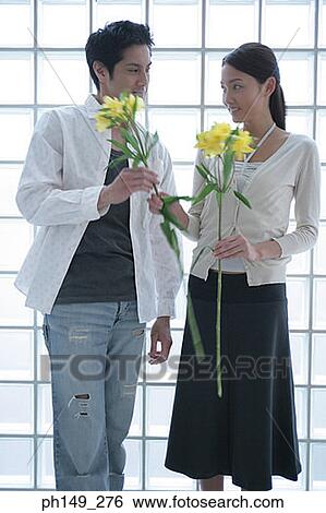 Close-up of a young couple holding flowers and looking at each other View Large Photo Image Stock Photograph - Close-up of a young couple holding flowers and looking at each other. Fotosearch