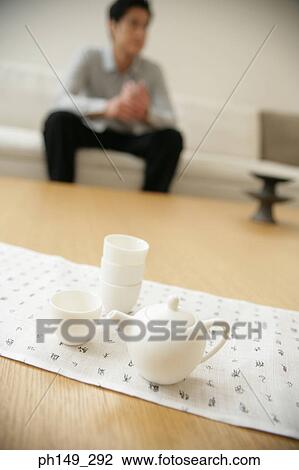 Stock Image - Close-up of cup and a kettle on the table with a man sitting in the background. Fotosearch