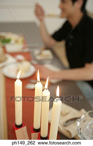 Close-up of four lit candles on a dining table with a man eating in the background View Large Photo Image Stock Image - Close-up of four lit candles on a dining table with a man eating in the background. Fotosearch