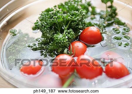 Stock Photo - Close-up of tomatoes and parsley with water in a bowl. Fotosearch