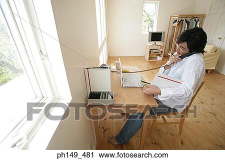 High angle view of a young man using a laptop and talking on the telephone View Large Photo Image Stock Image - High angle view of a young man using a laptop and talking on the telephone. Fotosearch