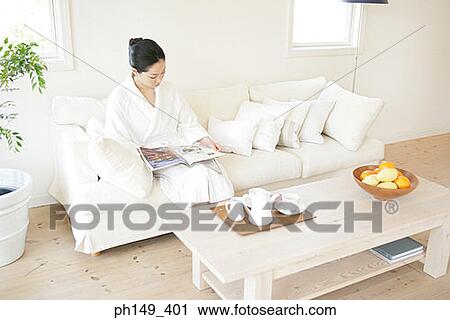 High angle view of a young woman sitting on a couch and reading a magazine View Large Photo Image Stock Image - High angle view of a young woman sitting on a couch and reading a magazine. Fotosearch