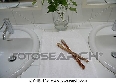 Stock Image - High angle view of two toothbrushes with a flower in a glass in the bathroom. Fotosearch