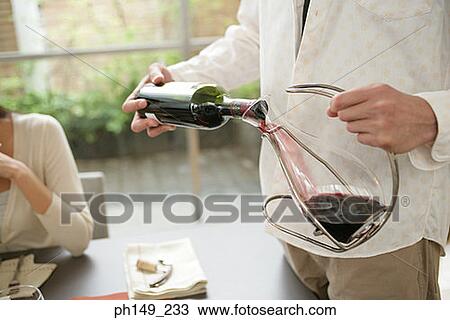 Mid section view of a man pouring red wine into a pitcher with a woman sitting at the dining table View Large Photo Image Stock Image - Mid section view of a man pouring red wine into a pitcher with a woman sitting at the dining table. Fotosearch