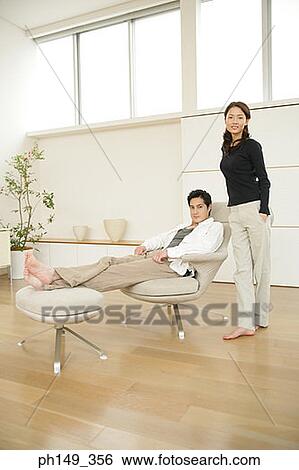 Portrait of a young man reclining in an armchair with a young woman standing beside him View Large Photo Image Stock Photograph - Portrait of a young man reclining in an armchair with a young woman standing beside him. Fotosearch