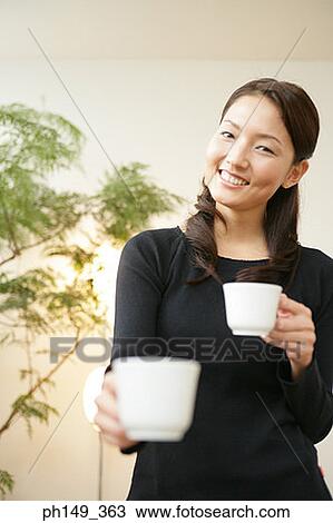 Stock Image - Portrait of a young woman holding coffee cups and smiling. Fotosearch