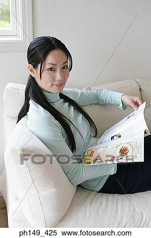 Portrait of a young woman sitting on a couch and holding a magazine View Large Photo Image Stock Photography - Portrait of a young woman sitting on a couch and holding a magazine. Fotosearch
