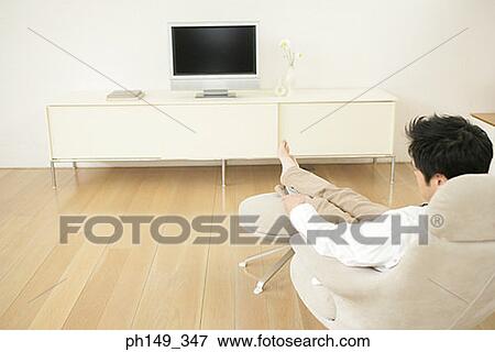 Rear view of a man sitting in an armchair in front of a television View Large Photo Image Stock Photo - Rear view of a man sitting in an armchair in front of a television. Fotosearch