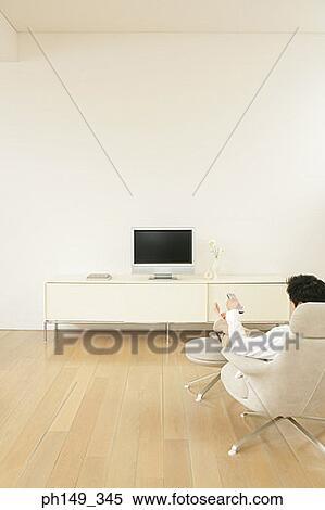 Stock Photography - Rear view of a man sitting in an armchair in front of a television. Fotosearch