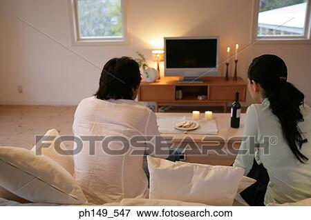 Rear view of a young couple sitting on a couch View Large Photo Image Stock Photo - Rear view of a young couple sitting on a couch. Fotosearch
