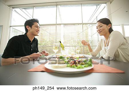 Picture - Side profile of a young couple sitting at the dining table. Fotosearch
