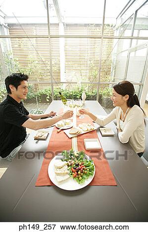 Side profile of a young couple sitting at the dining table and toasting wine glasses View Large Photo Image Stock Photo - Side profile of a young couple sitting at the dining table and toasting wine glasses. Fotosearch