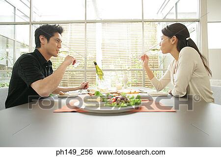 Side profile of a young couple sitting at the dining table and drinking white wine View Large Photo Image Stock Photograph - Side profile of a young couple sitting at the dining table and drinking white wine. Fotosearch