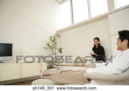 Side profile of a young man sitting in an armchair with a young woman holding a cup View Large Photo Image Stock Image - Side profile of a young man sitting in an armchair with a young woman holding a cup. Fotosearch