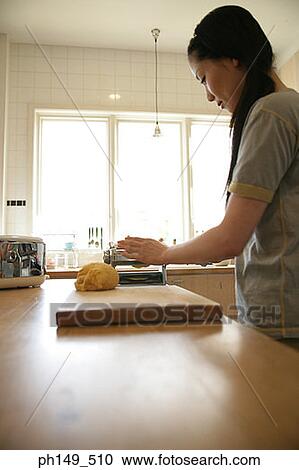 Stock Image - Side profile of a young woman preparing food in the kitchen. Fotosearch