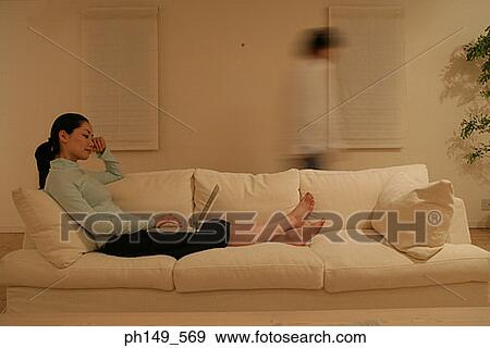 Side profile of a young woman reclining on a couch and using a laptop View Large Photo Image Stock Photo - Side profile of a young woman reclining on a couch and using a laptop. Fotosearch
