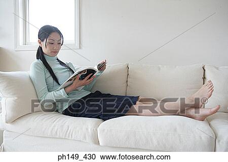 Side profile of a young woman sitting on a couch and reading a magazine View Large Photo Image Stock Image - Side profile of a young woman sitting on a couch and reading a magazine. Fotosearch