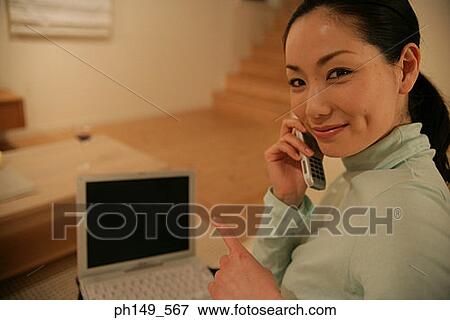 Side profile of a young woman talking on a mobile phone with a laptop on her lap View Large Photo Image Stock Photo - Side profile of a young woman talking on a mobile phone with a laptop on her lap. Fotosearch