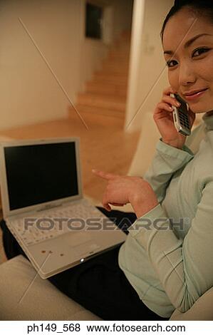 Side profile of a young woman talking on a mobile phone with a laptop on her lap View Large Photo Image Stock Photo - Side profile of a young woman talking on a mobile phone with a laptop on her lap. Fotosearch