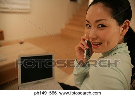 Side profile of a young woman talking on a mobile phone with a laptop on her lap View Large Photo Image Stock Photograph - Side profile of a young woman talking on a mobile phone with a laptop on her lap. Fotosearch