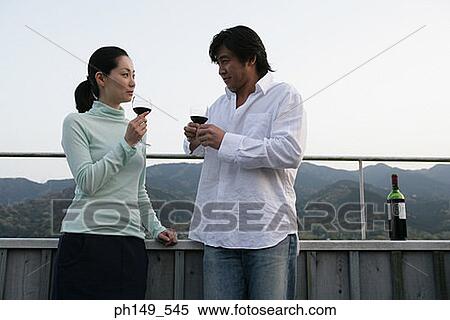 Stock Photography - Young couple holding wineglasses and looking at each other. Fotosearch