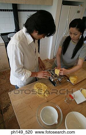 Stock Image - Young couple making noodles with the help of a pasta maker. Fotosearch