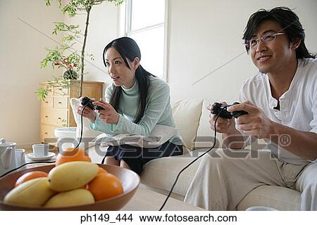 Young couple sitting on a couch and playing video games View Large Photo Image Picture - Young couple sitting on a couch and playing video games. Fotosearch