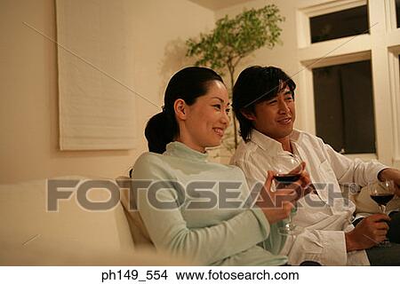 Young couple sitting on a couch and holding wineglasses View Large Photo Image Picture - Young couple sitting on a couch and holding wineglasses. Fotosearch