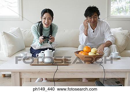 Young couple sitting on a couch and playing video games View Large Photo Image Stock Image - Young couple sitting on a couch and playing video games. Fotosearch