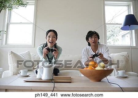 Young couple sitting on a couch and playing video games View Large Photo Image Stock Image - Young couple sitting on a couch and playing video games. Fotosearch