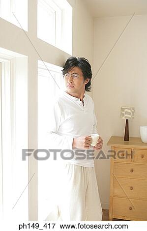 Young man holding a cup of tea and looking out of a window View Large Photo Image Stock Photo - Young man holding a cup of tea and looking out of a window. Fotosearch