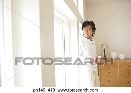 Stock Photo - Young man holding a cup of tea and looking out of a window. Fotosearch