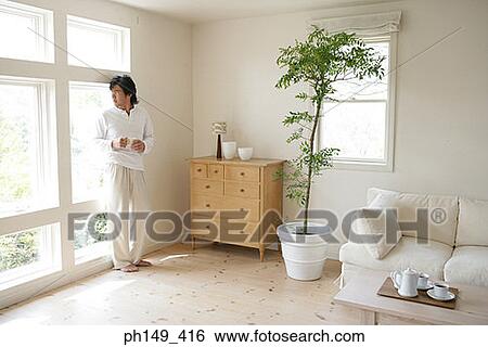 Stock Photograph - Young man holding a cup of tea and looking out of a window. Fotosearch