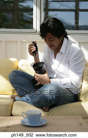 Young man sitting on a couch and cleaning a camera View Large Photo Image Stock Image - Young man sitting on a couch and cleaning a camera. Fotosearch