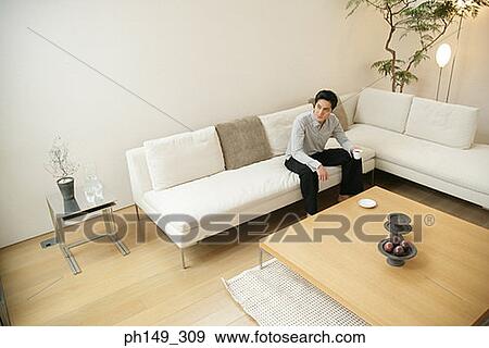 Stock Photo - Young man sitting on a couch and holding a cup of coffee. Fotosearch