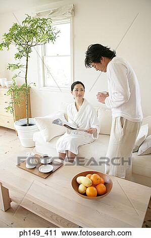Stock Image - Young man standing beside a young woman and reading a magazine. Fotosearch