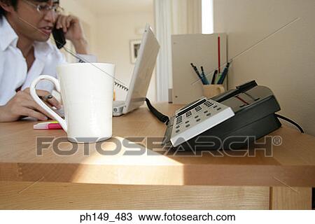Young man using a laptop and talking on the telephone View Large Photo Image Stock Image - Young man using a laptop and talking on the telephone. Fotosearch