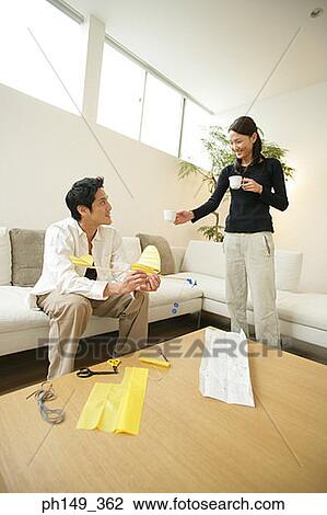 Stock Image - Young woman giving a cup of coffee to a young man holding a paper airplane. Fotosearch