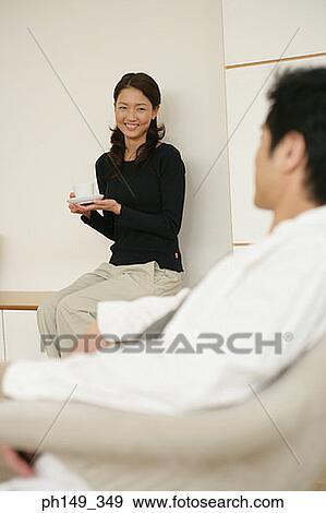 Young woman holding a cup and looking at a young man View Large Photo Image Stock Photo - Young woman holding a cup and looking at a young man. Fotosearch