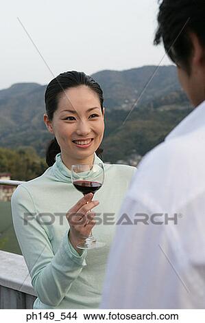 Young woman holding a wineglass and looking at a young man View Large Photo Image Picture - Young woman holding a wineglass and looking at a young man. Fotosearch