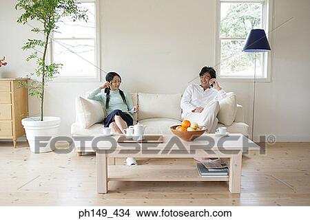 Young woman reading a magazine with a young man sitting beside her and talking on a mobile phone View Large Photo Image Picture - Young woman reading a magazine with a young man sitting beside her and talking on a mobile phone. Fotosearch