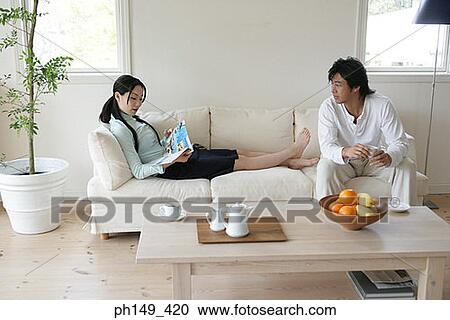 Stock Image - Young woman reading a magazine with a young man holding a cup of tea. Fotosearch