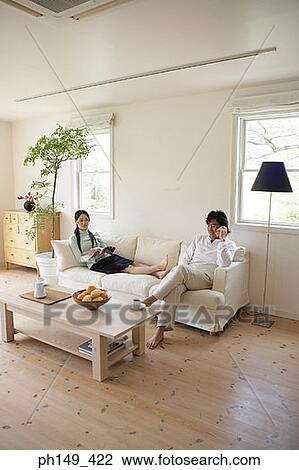 Young woman reading a magazine with a young man talking on a mobile phone View Large Photo Image Stock Image - Young woman reading a magazine with a young man talking on a mobile phone. Fotosearch