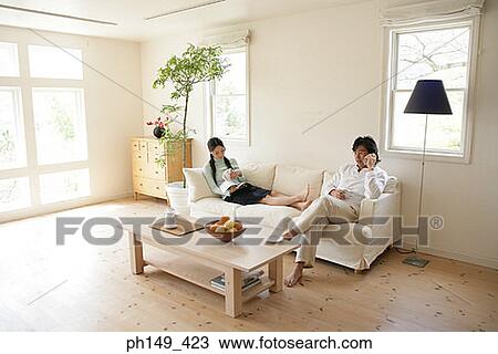 Young woman reading a magazine with a young man talking on a mobile phone View Large Photo Image Stock Image - Young woman reading a magazine with a young man talking on a mobile phone. Fotosearch