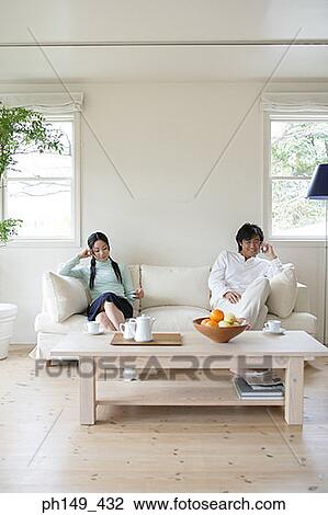 Young woman reading a magazine with a young man sitting beside her and talking on a mobile phone View Large Photo Image Stock Image - Young woman reading a magazine with a young man sitting beside her and talking on a mobile phone. Fotosearch