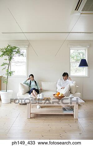 Stock Image - Young woman reading a magazine with a young man sitting beside her and talking on a mobile phone. Fotosearch