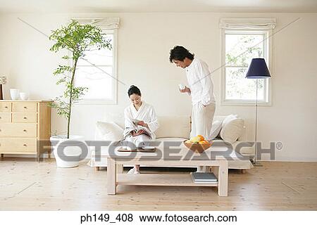 Young woman reading a magazine with a young man standing beside her and holding a tea cup View Large Photo Image Stock Photo - Young woman reading a magazine with a young man standing beside her and holding a tea cup. Fotosearch