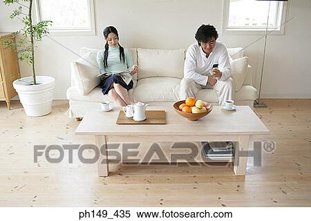 Young woman reading a magazine with a young man sitting beside her and holding a mobile phone View Large Photo Image Stock Photography - Young woman reading a magazine with a young man sitting beside her and holding a mobile phone. Fotosearch